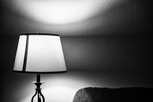 Black and white brightly illuminated electric lamp and lampshade in a darkened domestic home living room.