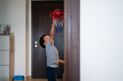 Experience the sheer excitement as a two and a half year old multiracial toddler achieves a slam dunk, skillfully throwing a ball into the basket in the hallway of his home. Watch the pure delight as the little one touches the hoop with triumphant glee
