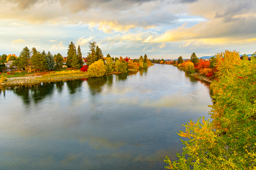 View of the Spokane River near the Barker Trail Head during Autumn, with fall colors on the leaves and sunlight and clouds reflecting in the water, in Spokane Valley, Washington, USA.