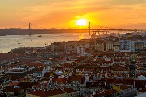 Sunset view of the Sanctuary of Christ the King monument and statue looking over the Tagus River and the Ponte 25 de Abril bridge from the Alfama district in Lisbon, Portugal.