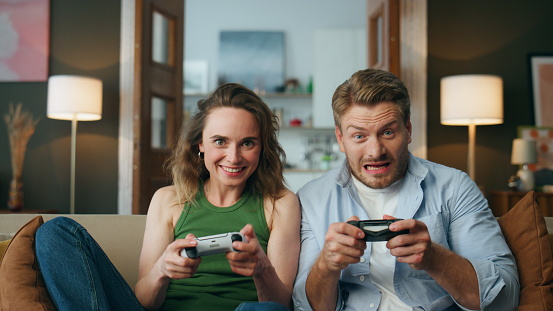 Overjoyed friends enjoy videogame activity home. Carefree pair holding gamepads