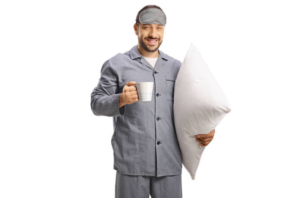 homme en pyjama avec un masque de sommeil tenant un oreiller et une tasse de boisson chaude - male mug shot cut out one person photos et images de collection