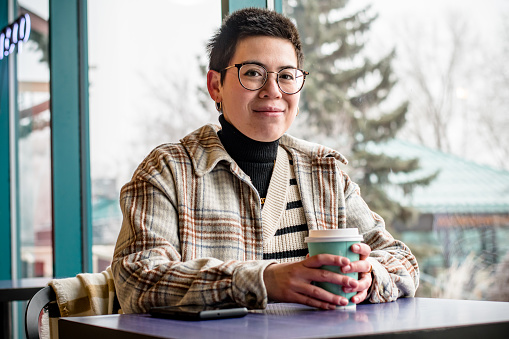 In an aura of cafÃ© elegance, a close-up captures a non-binary professional with autism and ADHD, savoring a cup of coffee, creating a moment of blissful indulgence in the soothing atmosphere