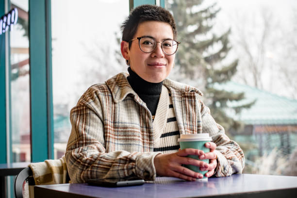 Connected Comfort: Non-Binary Professional Texting with Coffee at the Cafe In an aura of café elegance, a close-up captures a non-binary professional with autism and ADHD, savoring a cup of coffee, creating a moment of blissful indulgence in the soothing atmosphere happy and sad worker stock pictures, royalty-free photos & images