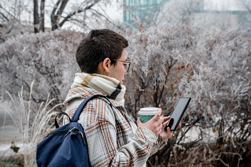 Embracing winter's beauty, a non-binary individual with autism and ADHD takes a tech-infused stroll, coffee and phone in hand, seamlessly blending the tranquility of nature with digital connectivity