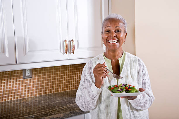 Mature African American woman eating salad in kitchen Mature African American woman eating healthy salad in kitchen black people eating stock pictures, royalty-free photos & images