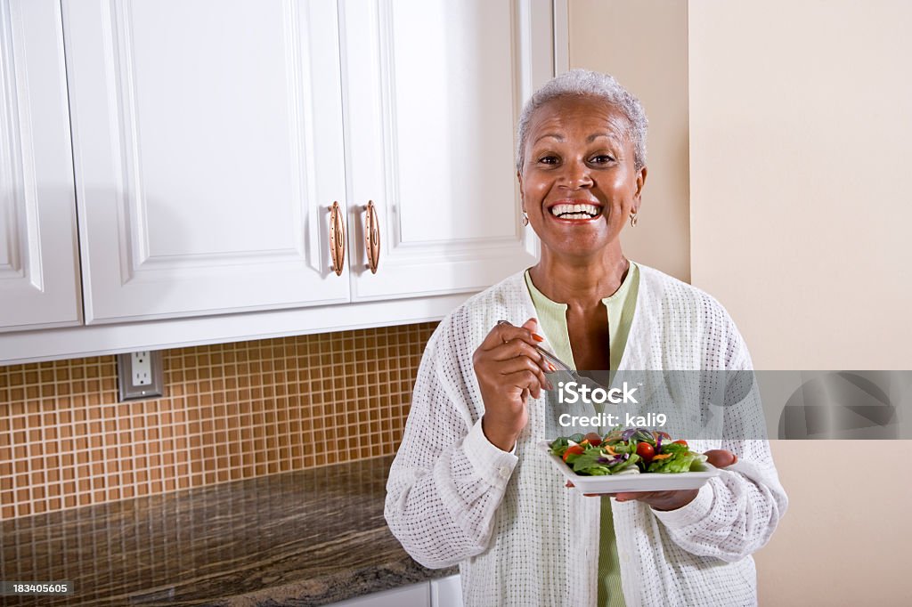 Madura afro-americana mulher comendo salada na cozinha - Foto de stock de Terceira idade royalty-free
