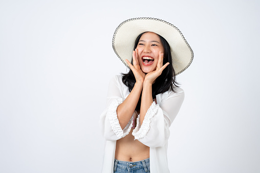 Young beautiful and cheerful Asian woman in summer clothes and a beach hat is posing cute on an isolated white background. summer vacation, holiday, beach trip, traveller