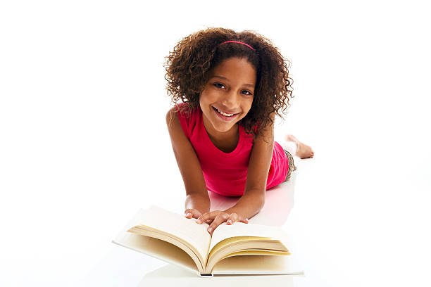 African ethnicity girl lying on front reading book "African ethnicity nine year old smiling and reading book, isolated on white background, copy space" 13 14 years child teenage girls lying down stock pictures, royalty-free photos & images