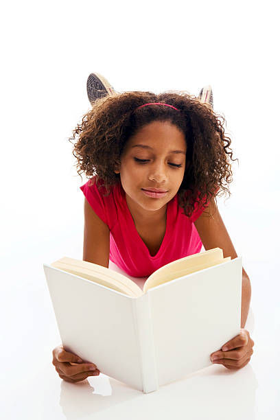 African ethnicity girl lying on front reading book "Nine year old female reading book, isolated on white background, copy space" 13 14 years child teenage girls lying down stock pictures, royalty-free photos & images