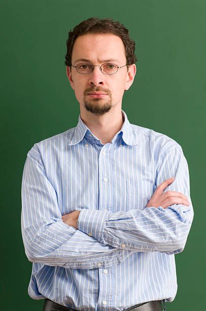 istock serious teacher with arms crossed at blackboard 183409069