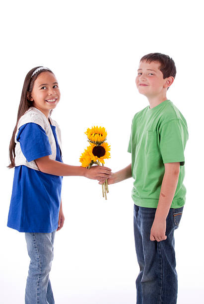 Funny kids are sitting on window sill, happy little boy giving a cute girl bouquet of pink tulip flower. Easter concept