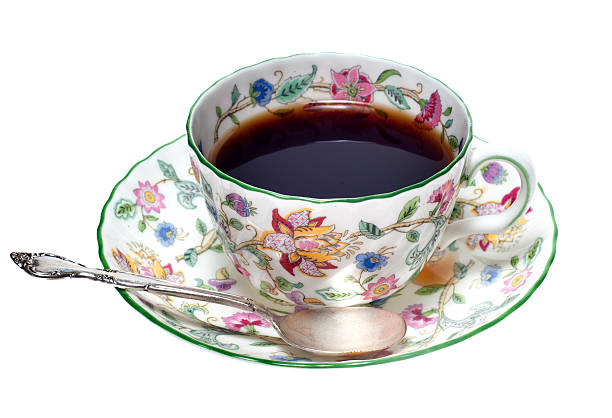 Empty cup of black tea on porcelain saucer with white ceramic spoon over vivid red paper background, close up, elevated top view, directly above