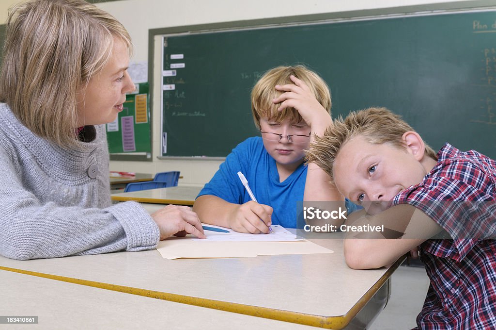Elementary school "teacher working with childrens in a classroom, one boy is thinking  hard, another one is  looking around and not paying attention." Homework Stock Photo