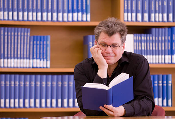 istock Older man with glasses reading a book in a library. 183410862