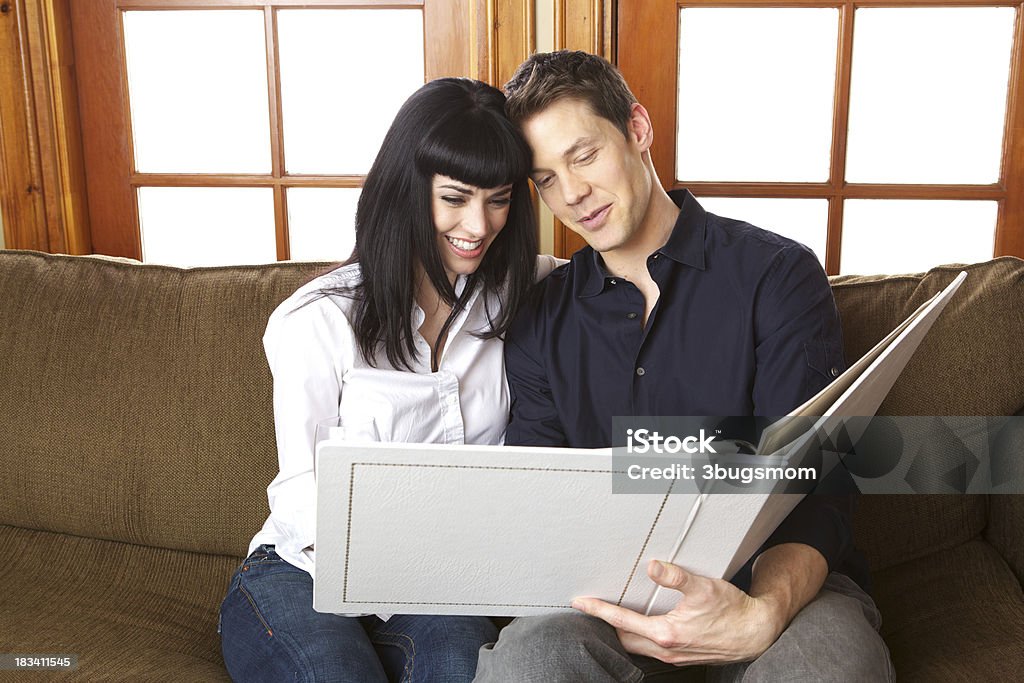 Beautiful Couple Looking at Their Wedding Album An attractive couple in their thirties sitting on a sofa smiling happily at their wedding album.  The woman has a glass of wine in her hand that is barely visible above the album 30-39 Years Stock Photo