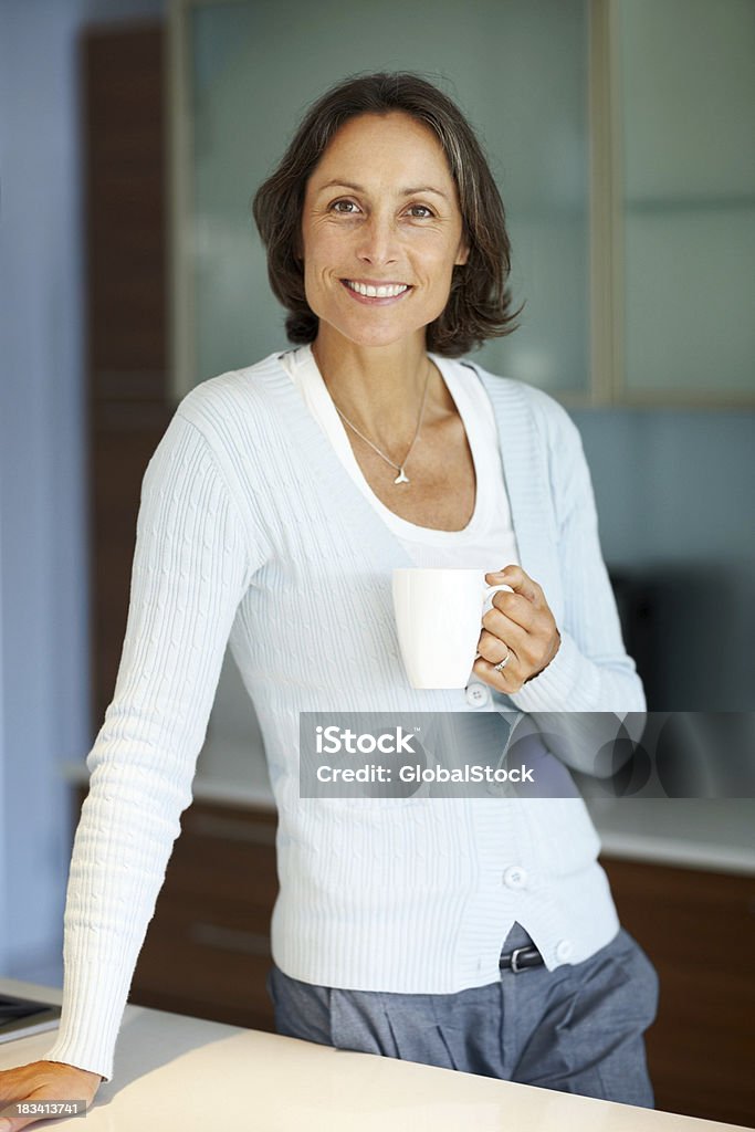 Tranquila mujer sosteniendo una taza de café en la cocina - Foto de stock de 40-49 años libre de derechos