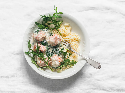 Orzo pasta with salmon meatballs in cream sauce with spinach  lunch on a light background, top view