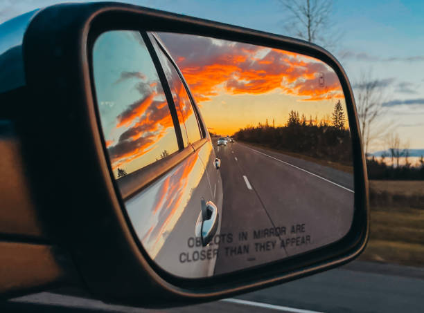 istock Sunset reflected in side mirror of vehicle on tree lined road. 1834143178