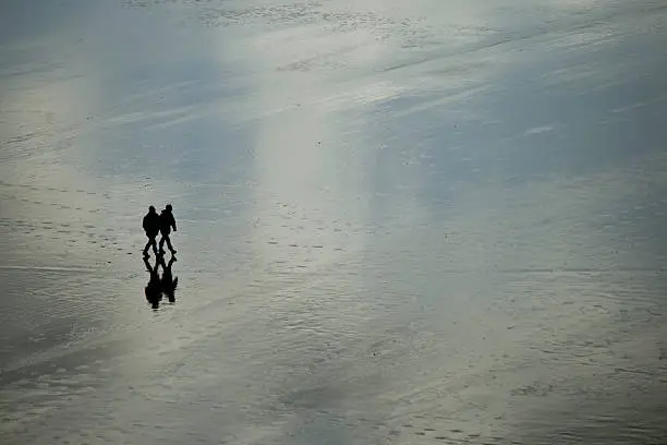Two people walk along Whitsand Beach in Cornwall during a cold and wet day in December.