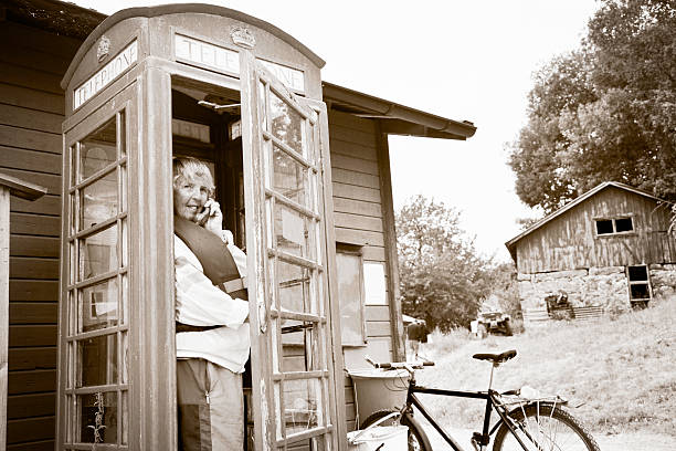 senior woman in a traditional English phonebox, photo taken in Sweden, sepia toning and texture added 