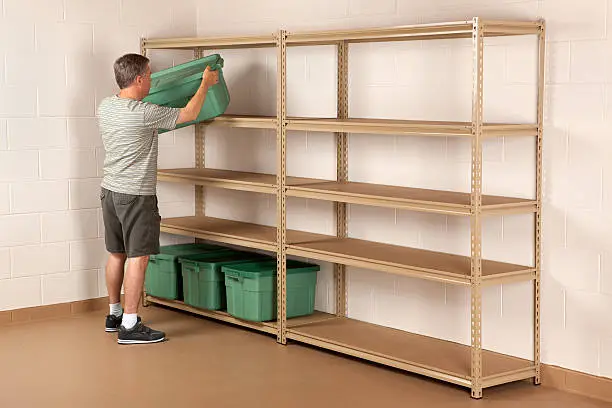 Man placing a plastic storage bin on a shelf in the basement.Please also see: