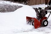 Close-up of red snowblower clearing snow-filled lane