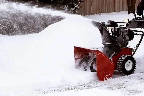 A red snowblower removing snow from a laneway blows the snow onto snowbanks.