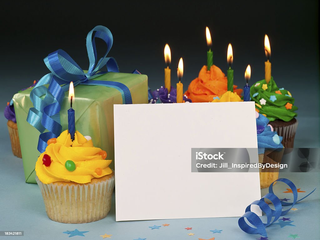 Celebration cupcakes with blank card Brightly colored Celebration cupcakes with blank a card that you can add your own message. Blank note card is made from recycled material and has flecks of fibers in the paper. Lit candles on the cupcakes. Birthday Cake Stock Photo