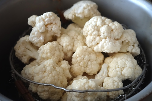 Cauliflower in pieces in a basket of a casserole dish for steaming