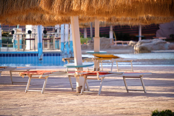 istock Empty deck chairs under straw shade umbrellas on swimming pool side in tropical resort. Summer vacations and getaway concept 1834230974