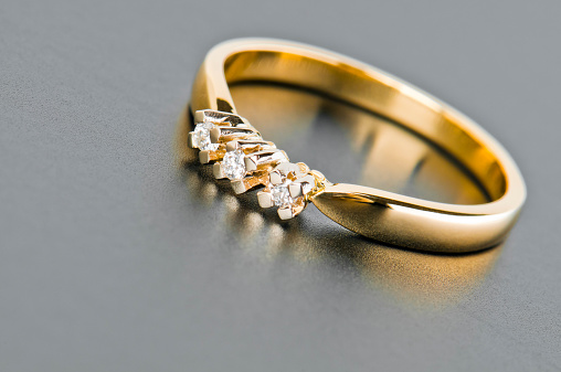 Close-up of single golden ring with three diamonds lying against solid gray background. Copy space, selective focus, studio shot.