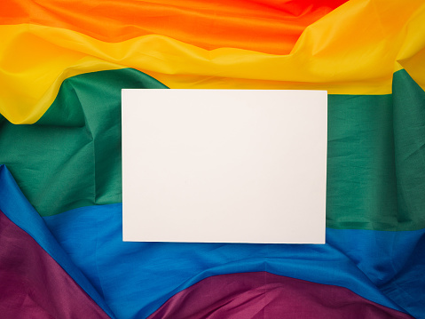 Top view of a blank white paper on the rainbow flag or LGBTQ flag background. Space for text. Top view. Flat lay. Gender diversity concept