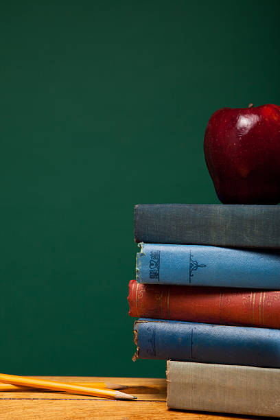 istock Apple and Old Books on School Desk by Chalkboard 183426470