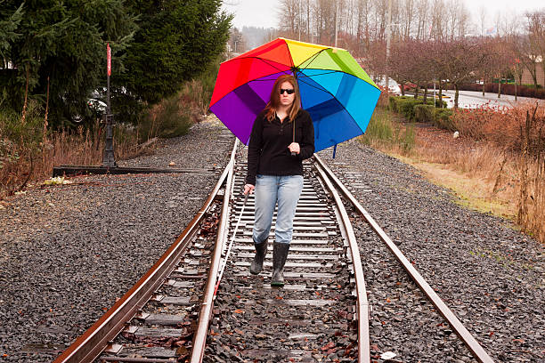 A cane user feels her way along railroad tracks in the rain.