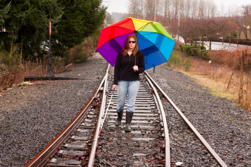 A cane user feels her way along railroad tracks in the rain.