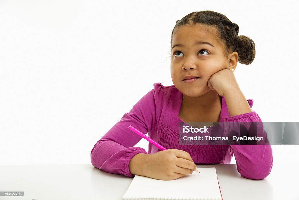 A girl thinking what to write in her notebook Black preschooler engrossed in writing something in her notebook. Isolated on white background Child Stock Photo