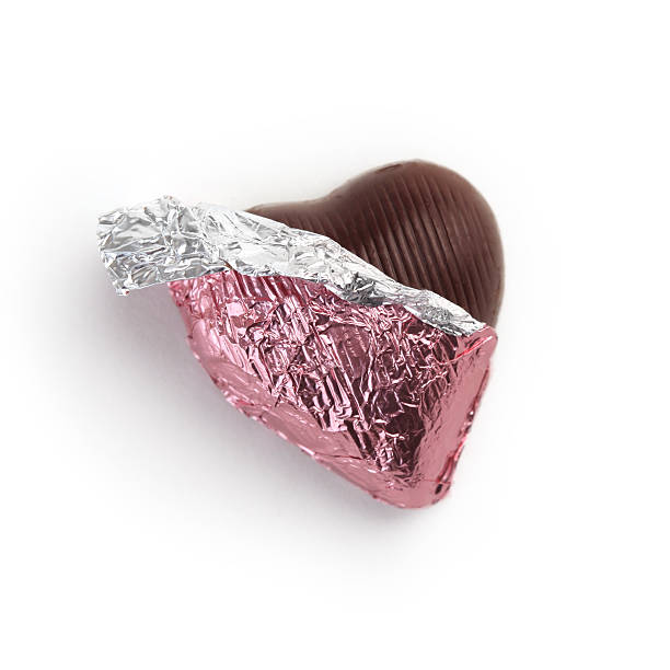 A foil-wrapped chocolate heart being unwrapped. White background.