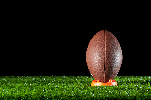 Gridiron ball standing on a tee on the grass at night