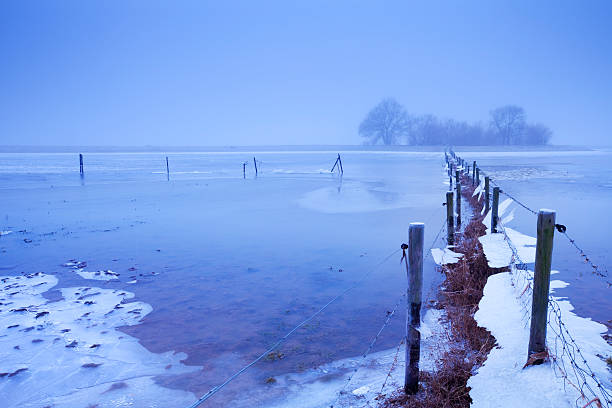 Flooded frozen floodplains at dawn, River Lek, The Netherlands "Flooded farmland with fences on the floodplains of a river. Photographed at dawn at a frosty, foggy morning." lek river in the netherlands stock pictures, royalty-free photos & images