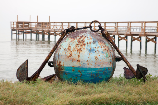 Old sphere shaped bouy and anchors on foggy morning beach at Rockport Texas