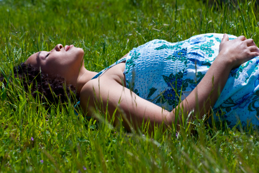 mixed race pregnant woman laying on green grass