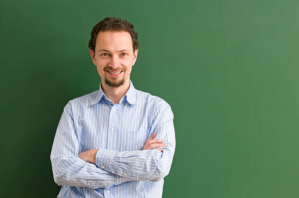 istock smiling teacher with arms crossed at blackboard 183433017