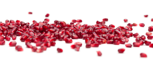 Red Pomegranate Seeds in a Bowl on a white wooden surface, top view. Flat lay, overhead, from above.