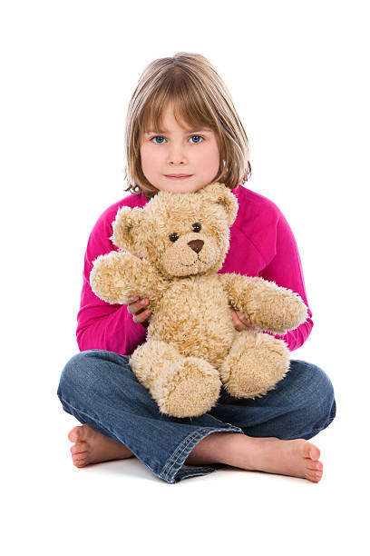 Close up portrait of cute little Asian girl in purple t-shirt sitting at playroom in her home, hugging a teddy bear and smiling and looking at camera, toys and scattered in the background