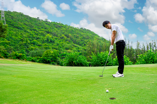 Closeup front view of an unrecognizable person hitting a putter near the hole.