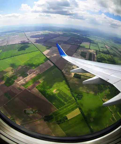 Photo of View of brown and green fields from an airplane porthole