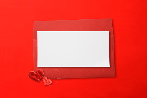 Close-up of red envelope with blank card and red sweet love heart shaped embroidery on red background.
