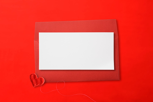 Close-up of red envelope with blank card and red sweet love heart shaped embroidery on red background.