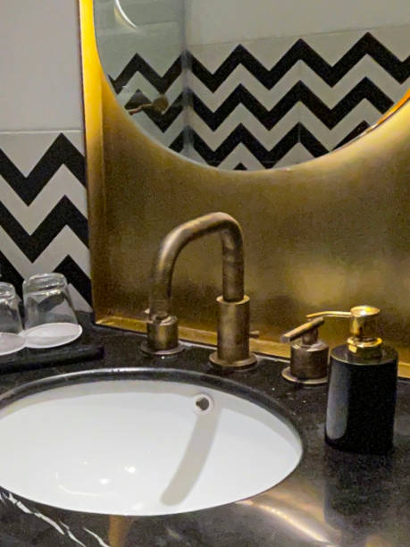 istock Close-up image of sink vanity unit, rolled face flannels on marble tray with upturned drinking glasses on marble bathroom counter, monochrome zig-zag patterned wall tiles, glass shower cubicle, mirror 1834467965